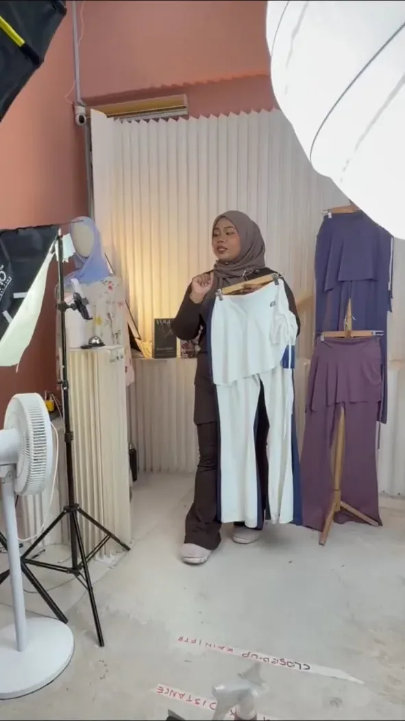 Host presenting an outfit beside a clothing rack in the studio
